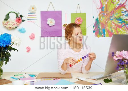 Attractive interior designer looking at computer screen with flat plan and choosing appropriate paint colors for wall decoration