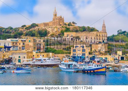 Beautiful cityscape over Gozo island with medieval architecture and passenger boats on the harbor - in Malta