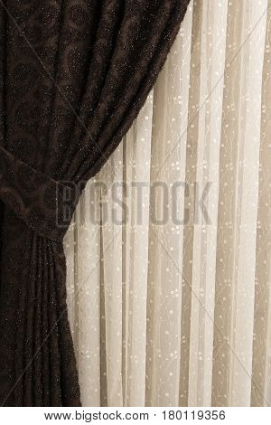 Beautifully draped long curtain on the window in the room. Close up of piled curtain. Luxury curtain home decor. Brown panels. White lace drapery