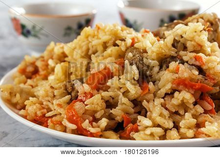 Friable pilaf with meat on a background of cups with tea. Closeup