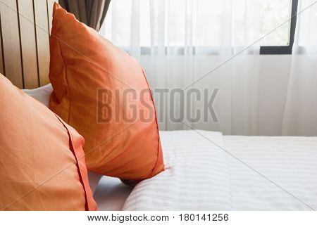 orange pillow and white blanket on bed in bedroom with lighting upper right side