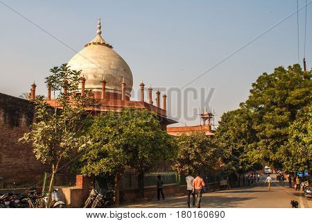 Taj Mahal in sun light with a little indian temple in the front. Early in the morning, back view behind the fence, from outside, street side with a siple indian life. Image with a blue sky. One of the most famous building in the world. This mausoleum was 