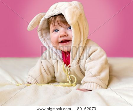 Beautiful infant lying on her belly and laughing on a pink background.