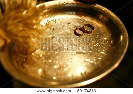 Gold wedding rings lie on a wet bronze tray