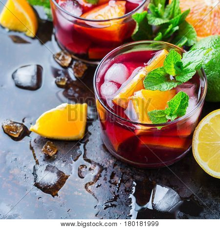 Traditional cold spanish sangria cocktail with red wine and ingredients on a black table citrus fruit orange lime lemon mint leaves and ice for hot summer days
