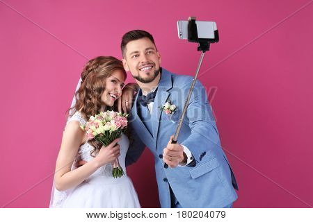 Happy wedding couple making selfie on color background