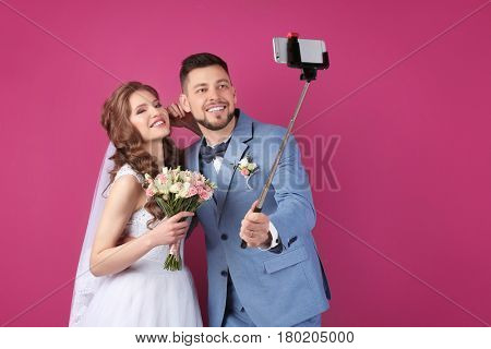 Happy wedding couple making selfie on color background