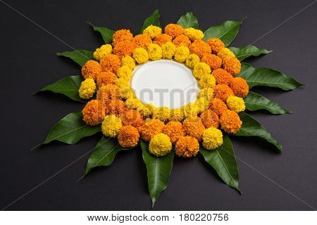 flower rangoli made using marigold or zendu flowers and mango leaves over black background with copy space in the middle, selective focus
