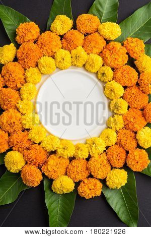 flower rangoli made using marigold or zendu flowers and mango leaves over black background with copy space in the middle, selective focus