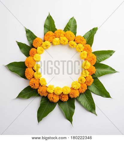 flower rangoli made using marigold or zendu flowers and mango leaves over black background with copy space in the middle, selective focus