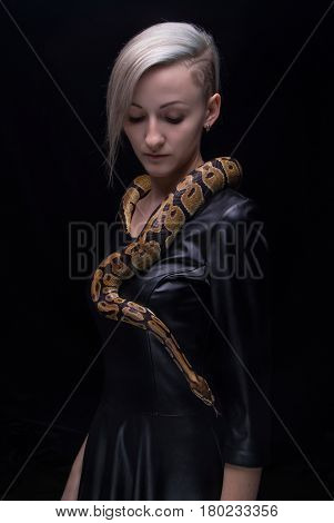Woman in leather dress with python on black background