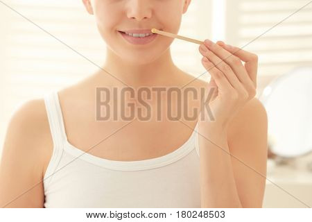 Young woman removing facial hair with wax on blurred background