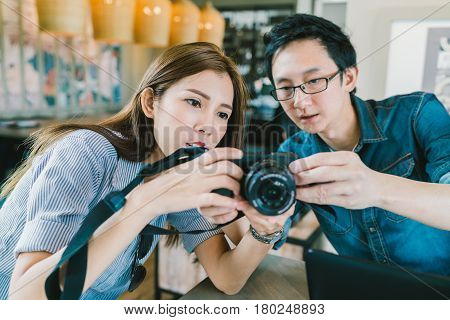Young Asian couple learning to use mirrorless digital camera together at coffee shop modern gadget technology concept focus on the girl depth of field effect
