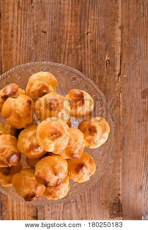 Sweet cream puffs in glass tray on wooden table.