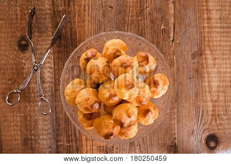 Sweet cream puffs in glass tray on wooden table.