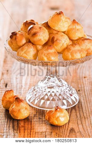 Sweet cream puffs in glass tray on wooden table.