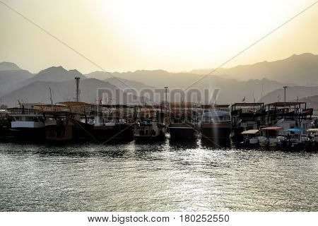 View on a boats docked at the little harbour in Oman beautiful sunset over Al Hajar Mountains