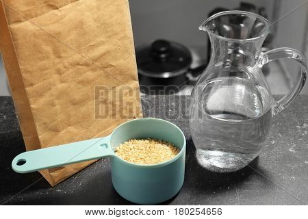 Measure scoop with brown rice and jug with water on kitchen table