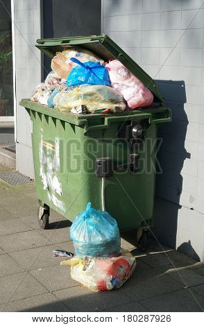 wheeled trash can container overflowing with garbage bags