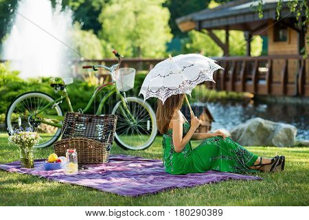 Beautiful young girl in spring dress sitting on picnic plaid. cute girl with umbrealla in hand on picnic in park. horizontal picture