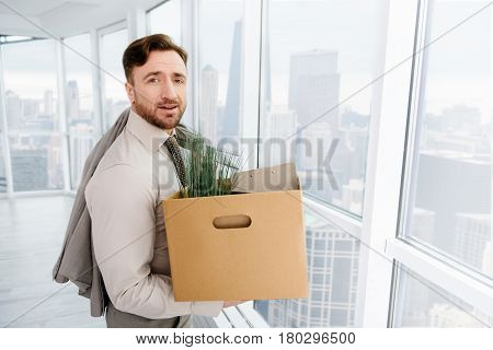 New period of life. Pleasant skillful employee holding box with his belongings and experincing first day at new workplace