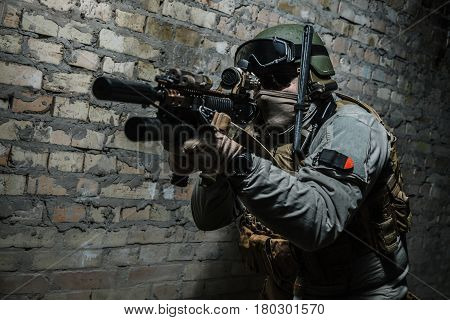 Special forces operator pointing weapon in the dark. Combat helmet, tactical radio system with folding antenna are on. Low key image