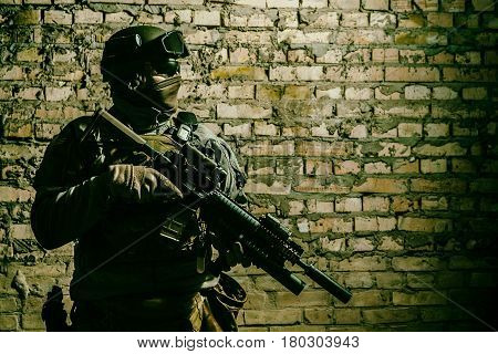 Special forces operator pointing weapon in the dark. Combat helmet, and bulletproof vest are on. Low key image, shadow soldier