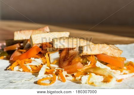 Roasted tofu and fresh vegetables on flat bread. Ingredients of vegan rolled sandwich on lavash bread in natural light