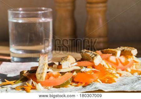 Roasted tofu and fresh vegetables on flat bread on kitchen table. Ingredients of bean curd vegan rolled sandwich on lavash bread in natural light