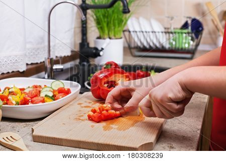 Child hands chopping a red bellpepper for a fresh vegetables salad - closeup on a kitchen sink area with all the ingredients