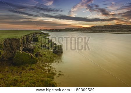 The river Ogmore, south Wales, at sunset. A slow shutter speed has smoothed out the river and the river bank looks to be eroding