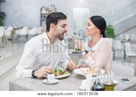 Date in luxury restaurant. Lovely couple in cafe with stylish interior. Man and woman having delicious meal. Woman giving food to man