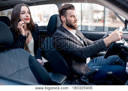 Businesswoman on the backseat with elegant man driving a car in the city. Worried about a delay to an important meeting