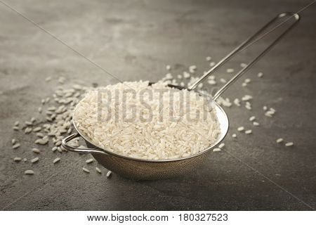 Metal sieve full of rice on grey table