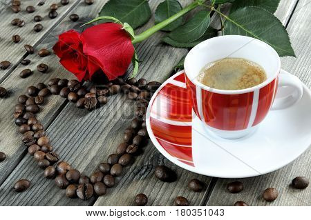 Aromatic Italian style coffee served in a beautiful red cup on a wooden table old adorned with a red rose and coffee beans.