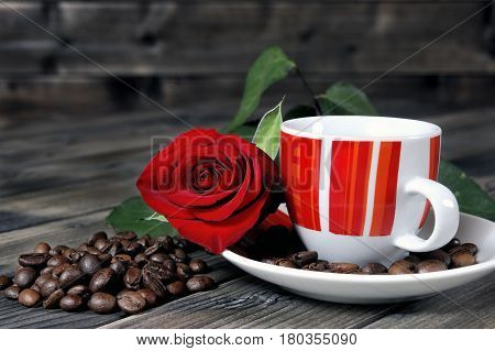 Aromatic Italian style coffee served in a beautiful red cup on a wooden table old adorned with a red rose and coffee beans.