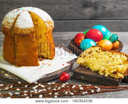 Easter sweet bread Orthodox kulich paska willow twigs. Easter Colorful eggs on gray wooden background. Holidays breakfast. Palm Sunday. Space for text.