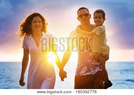 Happy family of father, mother and young son is walking on sunsset beach background