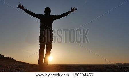 freedom. Man stands on a cliff sunset silhouette hand in sides lifestyle