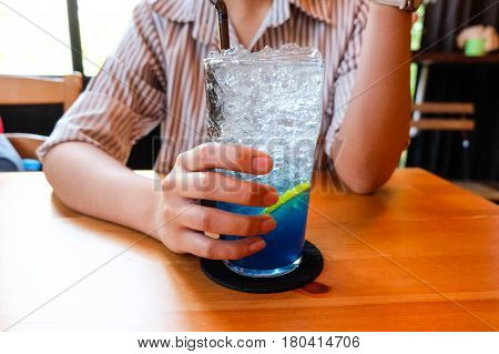 Young woman handle glass of splash blue lemon juice soda on the wood table suumer and fresh concept