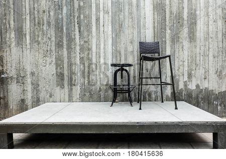 short circle and long square metal chairs on the stage with cement wall background stand by or lonele concept