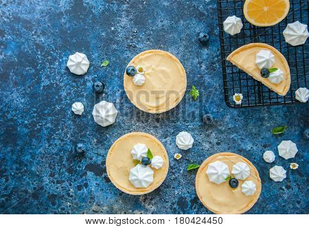 Whole And Slice Of Individual Lemon Curd Tarts With Blueberry Jam Meringue And Basil Leaves On A Blu