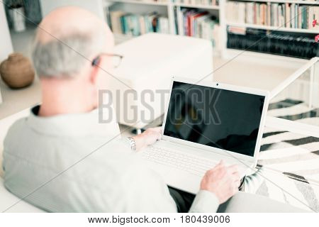 Man On Couch With Laptop At Home. Over Shoulder Shot.