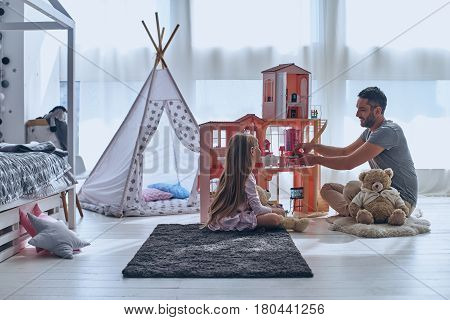 Using imagination. Father and daughter playing with a dollhouse together while sitting on the floor in bedroom