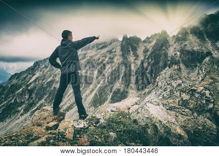 Hiker stays on a rocky ridge and point to the sunrise over the mountain. Caucasian Georgia Swaneti region.