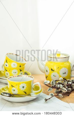 Elegant yellow tea set with floral ornament on aged wood table bouquet of willows spring Easter branch or tea party sunlight