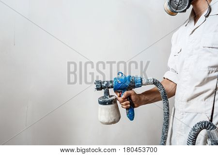 Worker painting wall with spray gun in white color. Copy space.