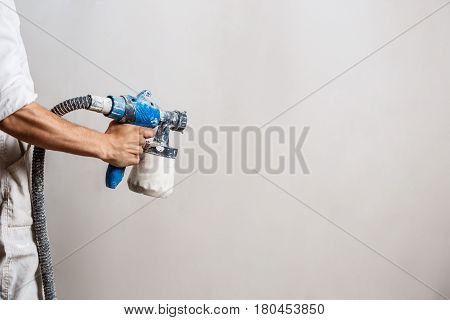 Worker painting wall with spray gun in white color. Copy space.