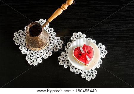 Jezva with coffee saucer with red heart-shaped gingerbread on a black wooden background. Top view
