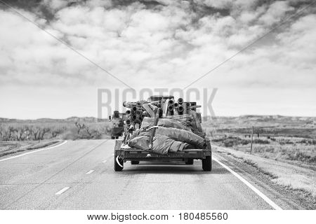 A flat bed trailer loaded with industrial hoses and tarps travelling down a highway in a black and white rocky landscape